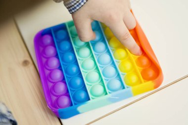 Çocuk duyusal oyuncak Pop-it ile oynuyor. Kaliteli motor becerileri için araç, saymaya başlamak için araç, birincil aritmetik işlemlerini öğrenmek. Parmak uyumu ve rahatlama için bir yatıştırıcı..