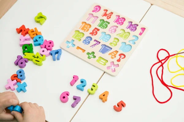 Çocuk oyun yoluyla numaraları öğreniyor. Tahta sayılar ve ayakkabı bağcıklarıyla duyusal aktivite. Evde eğitim, okul öncesi eğitim, Montessori metodolojisi. sayılar dizisi, aritmetik problemler.