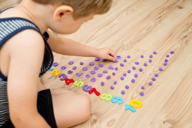 Play-Doh taşları ve numaraları. DIY oyunu sayılıyor. Matematiksel bir görev. Evde oyna. Öğrenmenin bir yolu. Çocuk bir rakam söylerken topları düzleştirdi.