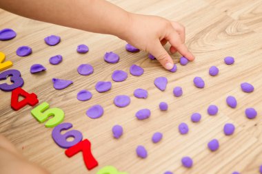 Play-Doh taşları ve numaraları. DIY oyunu sayılıyor. Matematiksel bir görev. Evde oyna. Öğrenmenin bir yolu. Çocuk bir rakam söylerken topları düzleştirdi.