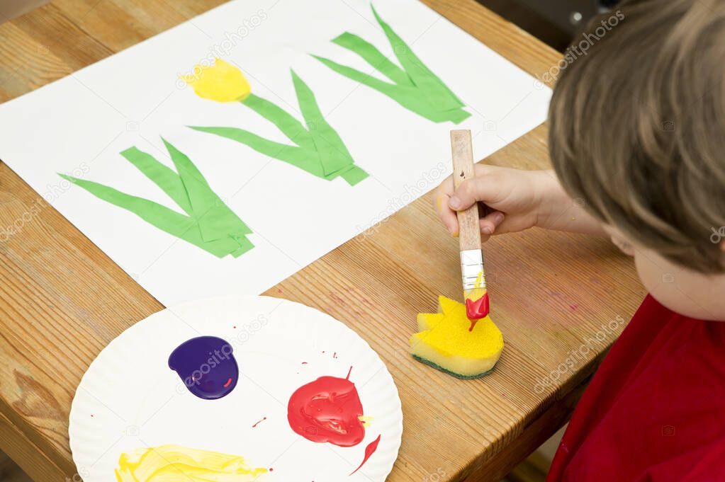 Kid painting with gouache a spring flower. Boy produces colored tulips for mommy. Children's activities, easy ideas for children at home. Art lessons at home. DIY tasks for children. Early education.