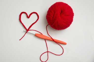 Beyaz arka planda yün bir top ve kalp şeklinde yakın plan. Kalp şeklinde yün iplik. Aşk Tığ işi.