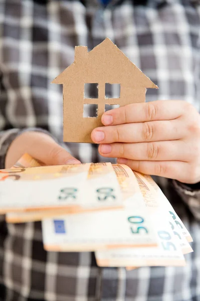 Saving money for a dream house. Child in one hand holds Euro in other cardboard house. Loan for new house theme. Credit, debt, Financial operations. Smart investment.