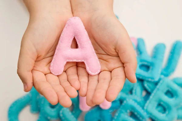 Stuffed felt letter of the alphabet in open hands of child. Kid holding handmade capital letters 