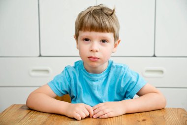 Okula dönelim. Çocuk kreşte ya da anaokulunda masanın yanında oturuyor. Duygular. Mutlu yüz ifadesi. Avuç içleri açık gülümseyen çocuk.