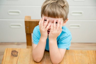 Okula dönelim. Çocuk kreşte ya da anaokulunda masanın yanında oturuyor. Duygular. Mutlu yüz ifadesi. Avuç içleri açık gülümseyen çocuk.