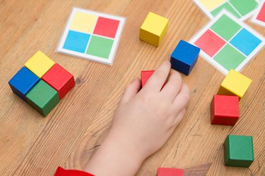 Çocuk mantıklı bir oyun oynuyor. Diziyi tekrarla. Kaplamalı kağıttaki renkli kareler. Görevi tamamlamak için tahta küpleri. Montessori tipi eğitim oyuncağı. Güzel motor beceriler. Çocuk Geliştirme.