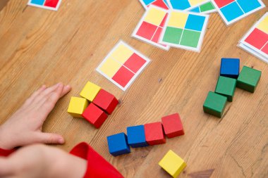 Çocuk mantıklı bir oyun oynuyor. Diziyi tekrarla. Kaplamalı kağıttaki renkli kareler. Görevi tamamlamak için tahta küpleri. Montessori tipi eğitim oyuncağı. Güzel motor beceriler. Çocuk Geliştirme.
