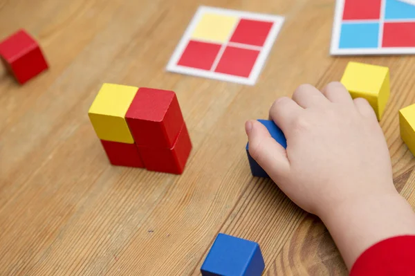 Kid playing logical game. Repeat the sequence. Color squares on laminated paper. Wooden cubes to achieve task. Montessori type educating toy. Fine motor skills. Child Development.