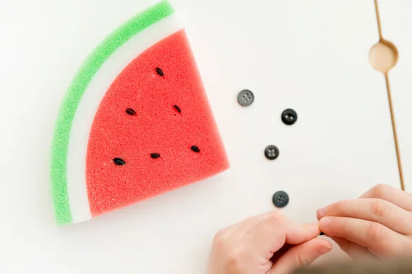 Watermelon shape sponge stuffed with plastic button. Montessori tool for training fine motor skills, hand coordination, focus, patience. Sensory therapy, early education.