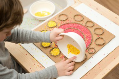 Çocuk renkli pirinçle oynuyor. Çocukların oyun yoluyla iyi motor becerileri geliştirmesi için uygulama. El-göz koordinasyonunu öğrenmek için oyuncak. Evde Montessori tipi anaokulu aktiviteleri.