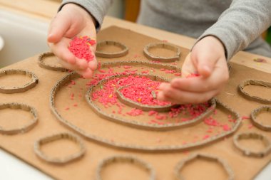 Çocuk renkli pirinçle oynuyor. Çocukların oyun yoluyla iyi motor becerileri geliştirmesi için uygulama. El-göz koordinasyonunu öğrenmek için oyuncak. Evde Montessori tipi anaokulu aktiviteleri.
