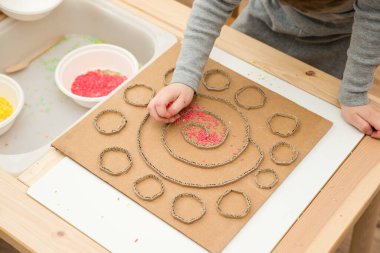 Çocuk renkli pirinçle oynuyor. Çocukların oyun yoluyla iyi motor becerileri geliştirmesi için uygulama. El-göz koordinasyonunu öğrenmek için oyuncak. Evde Montessori tipi anaokulu aktiviteleri.