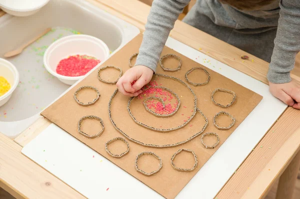 Çocuk renkli pirinçle oynuyor. Çocukların oyun yoluyla iyi motor becerileri geliştirmesi için uygulama. El-göz koordinasyonunu öğrenmek için oyuncak. Evde Montessori tipi anaokulu aktiviteleri.