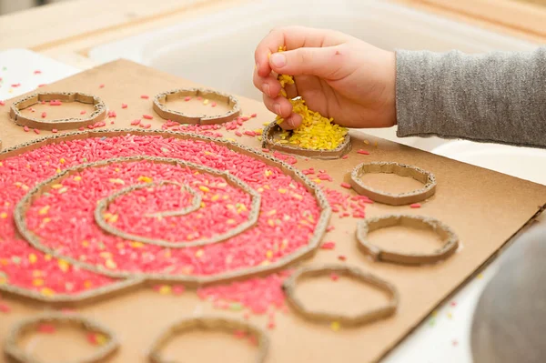 Çocuk renkli pirinçle oynuyor. Çocukların oyun yoluyla iyi motor becerileri geliştirmesi için uygulama. El-göz koordinasyonunu öğrenmek için oyuncak. Evde Montessori tipi anaokulu aktiviteleri.