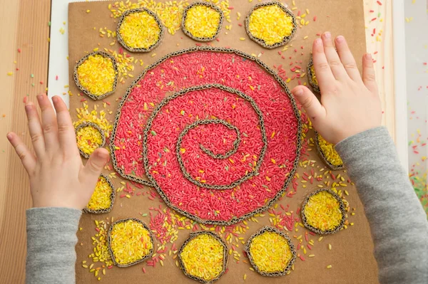 Boy plays with colored rice. Implement for children to develop fine motoric skills through play. DIY toy to learn hand - eye coordination. Montessori type pre school activities at home.