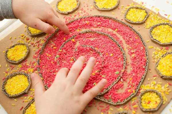 Çocuk renkli pirinçle oynuyor. Çocukların oyun yoluyla iyi motor becerileri geliştirmesi için uygulama. El-göz koordinasyonunu öğrenmek için oyuncak. Evde Montessori tipi anaokulu aktiviteleri.