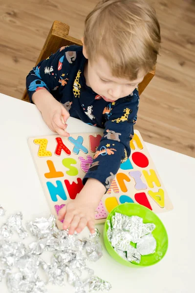 Two year boy playing with wooden alphabet letters board. Letters wrapped in foil. Intellectual game, preschool implement for early education. Verbal and memory training exercise.