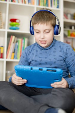 Mavi elbiseli çocuk yerde oturuyor ve mavi iPad 'le oynuyor..