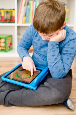 Mavi elbiseli çocuk yerde oturuyor ve mavi iPad 'le oynuyor..