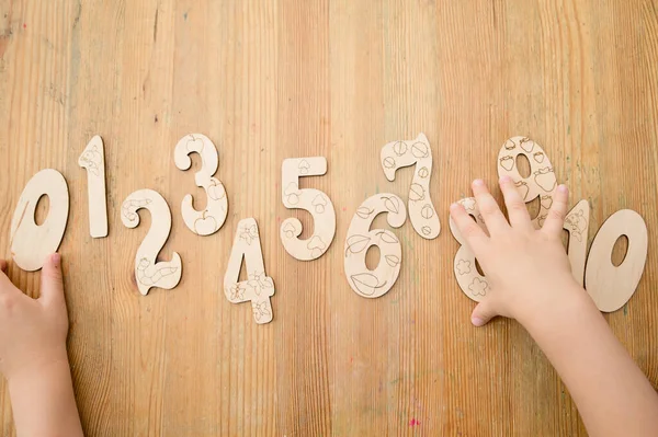 Wooden jigsaw digits from 0 to 10 on natural wood table. Learning numbers. Toy for preschool Kids. Boy pointing number six. Implement for nursery or kindergarten.