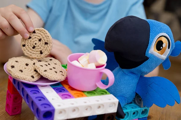 Kid plays role game. Tea time with best friend. Toy parrot sitting by the table. Activities at home. Indoor games for rainy day.