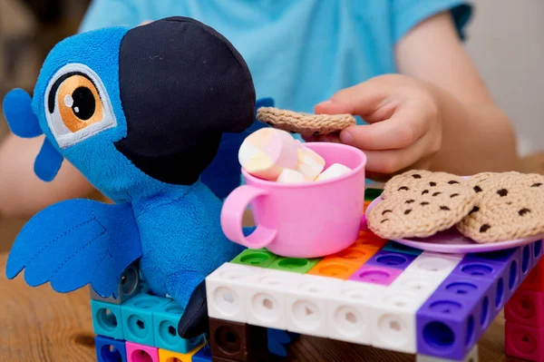 Kid plays role game. Tea time with best friend. Toy parrot sitting by the table. Activities at home. Indoor games for rainy day.