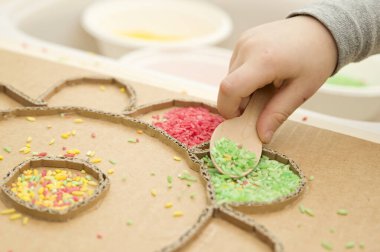 Çocuk renkli pirinçle oynuyor. Çocukların oyun yoluyla iyi motor becerileri geliştirmesi için uygulama. El-göz koordinasyonunu öğrenmek için oyuncak. Evde Montessori tipi anaokulu aktiviteleri.