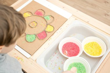 Çocuk renkli pirinçle oynuyor. Çocukların oyun yoluyla iyi motor becerileri geliştirmesi için uygulama. El-göz koordinasyonunu öğrenmek için oyuncak. Evde Montessori tipi anaokulu aktiviteleri.