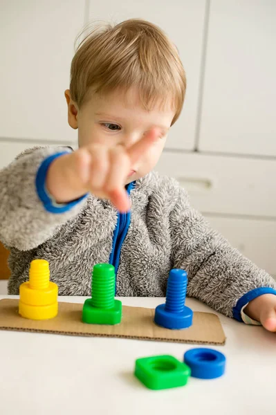 Shapes, colors and fine motor skills. toddler turns the nut on the bolt. Task to twist correct color part on matching thread. expressive child mimic, concentrated, involvement in the process.