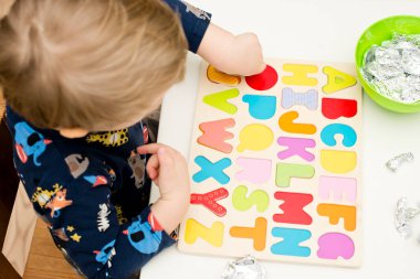 Tahta alfabe harfleriyle oynayan iki yaşında bir çocuk. Folyoya sarılı mektuplar. Entellektüel oyun, erken eğitim için anaokulu uygulaması. Sözlü ve bellek alıştırması.
