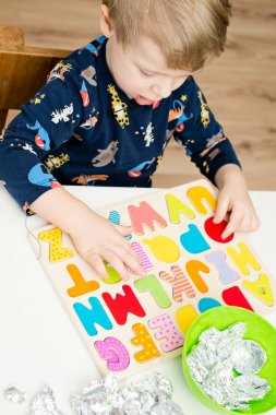 Tahta alfabe harfleriyle oynayan iki yaşında bir çocuk. Folyoya sarılı mektuplar. Entellektüel oyun, erken eğitim için anaokulu uygulaması. Sözlü ve bellek alıştırması.