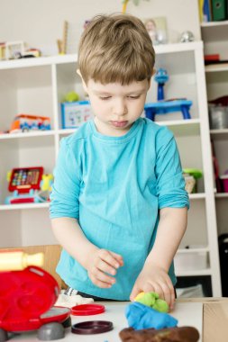 Oyun hamuruyla yemek pişirmek. Çocuk farklı renkte plastiklerle ve plastik mutfak malzemeleriyle oynuyor. Küçük çocuğun sanatsal yüz ifadesi.