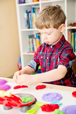 Oyun hamuruyla yemek pişirmek. Çocuk farklı renkte plastiklerle ve plastik mutfak malzemeleriyle oynuyor. Küçük çocuğun sanatsal yüz ifadesi.
