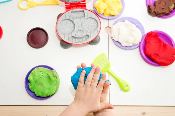 Cooking with play dough. Kid plays with different color plasticine and plastic kitchen equipment. Artistic face expression of little boy.