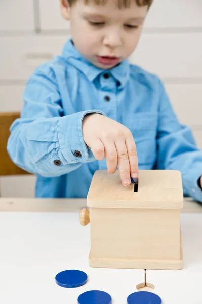 Money-box. Young economist inserts toy coins in wooden money saving box. Investment, economy, inflation, banking. Retirement saving and pension planning. Money generation, business language.