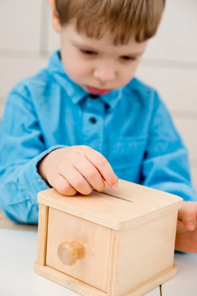 Money-box. Young economist inserts toy coins in wooden money saving box. Investment, economy, inflation, banking. Retirement saving and pension planning. Money generation, business language.