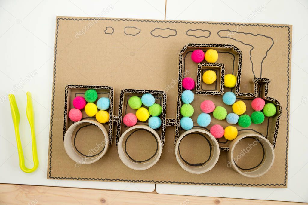 Pompom train. 3D train board for active brain exercise game made from paper core tubes and cardboard. Montessori methodology task to sort different colors.