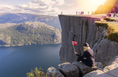 Norveç bayrağı taşıyan sarışın turist preikestolen manzarasına bakıyor. Turist eğlencesi. Dağlarda güneşli bir hava - Norveç