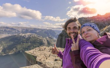 Kürsü Kayası 'nın (Preikestolen) zirvesinde dünyanın en muhteşem izleme noktalarından biri olan neşeli bir çift. Lysefjord, Norveç 'ten 604 metre yüksekte bir plato.