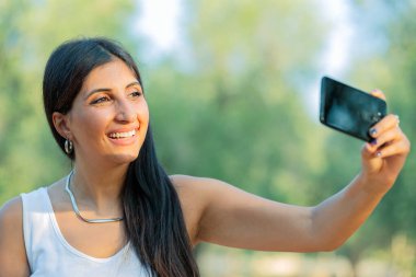 güzel genç kadın kendini telefon ile fotoğraf çekmek. bir selfie, açık havada güneşli bir yaz günü alarak tatlı gülümseyen genç beyaz genç kız