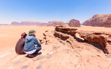 Bir turist yerel rehberiyle Ürdün 'deki Wadi Rom çölündeki taş kemere bakıyor. Mavi gökyüzü