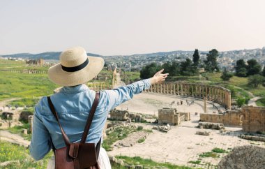 young woman tourist in color dress and hat enjoying the Oval Forum in ancient Roman city Gerasa, present-day Jerash, Jordan