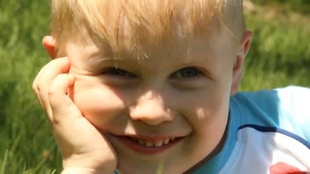 Smiling blond boy on a background of green grass. — Stock Video