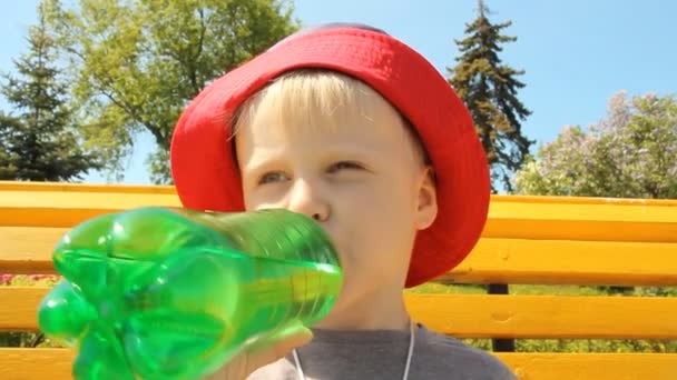 Usměvavý chlapeček v panama hat pije vodu z láhve. Procházka v parku — Stock video