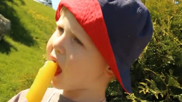 Ein kleiner Junge isst Eis im Panamahut vor dem Hintergrund der Natur — Stockvideo