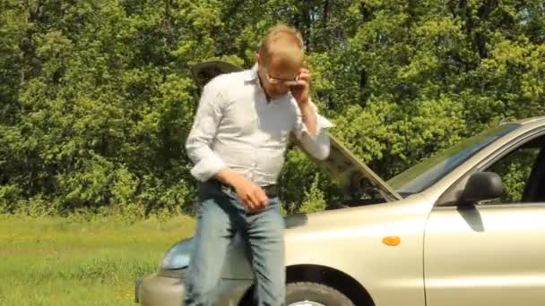 Hombre hablando por teléfono en la capucha abierta de un coche roto — Vídeo de stock