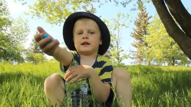 Kleiner Junge auf der Wiese trinkt Wasser — Stockvideo