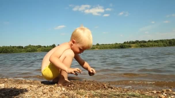 Маленький хлопчик грає на березі озера. Вода відпочинку — стокове відео