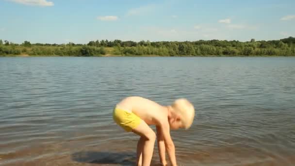 Kleine jongen spelen op de oever van het meer. Waterrecreatie — Stockvideo